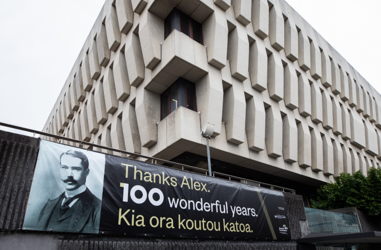 Wide-angle view of the National Library building corner with new banner hanging on wall outside which reads: Thanks Alex. 100 wonderful years. Kia ora koutou katoa.