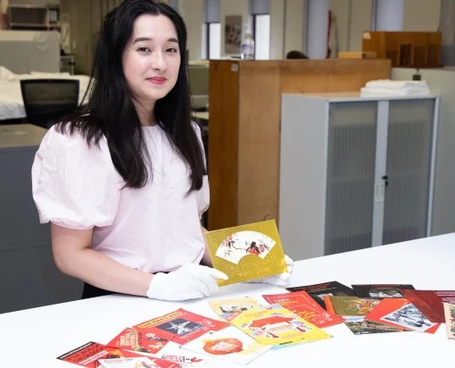 A woman wearing white gloves holds collection items with others displayed on table in front of her. 