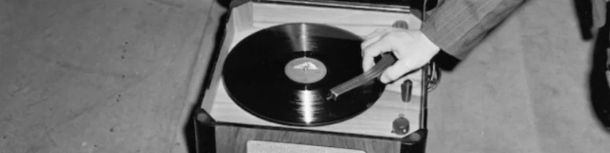 A gramophone with a record in it. A hand is lowering the tonearm.
