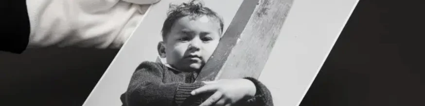 Gloved hands holding a photograph of a young, shy Māori boy.
