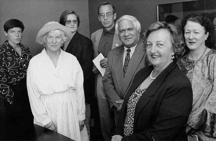 Black and white photo of 7 people wearing formal clothing, posing for the camera.