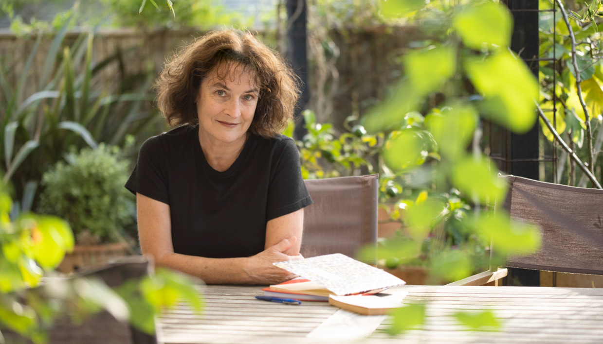 Kate De Goldi sitting at a table in a garden.