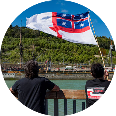 Protest looking over a harbour at a ship. They are waving the United Tribes flag. 