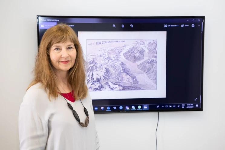 A woman stands in front of a wall-mounted screen showing a drawing of a New Zealand alpine environment.