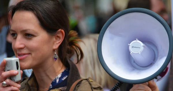 Woman with brown hair speaking into a megaphone microphone. 
