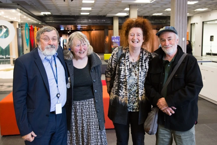 A group portrait of four people smiling and standing on the ground floor of the National Library building.