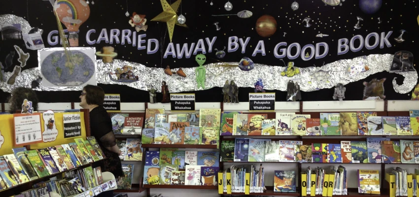 Books displayed on shelves with background mural of planets in space with the words: 'Get carried away by a good book'