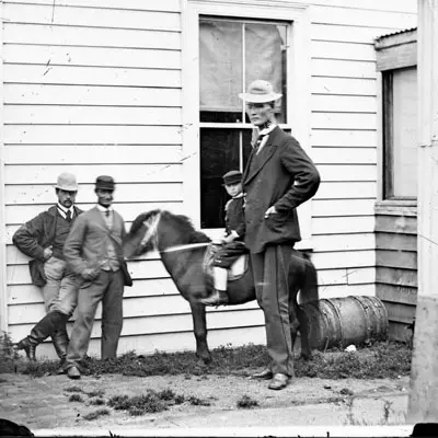 Victorian era black and white photo. Three men and a boy on a pony in front of a weatherboard house. One of the men is very tall. 