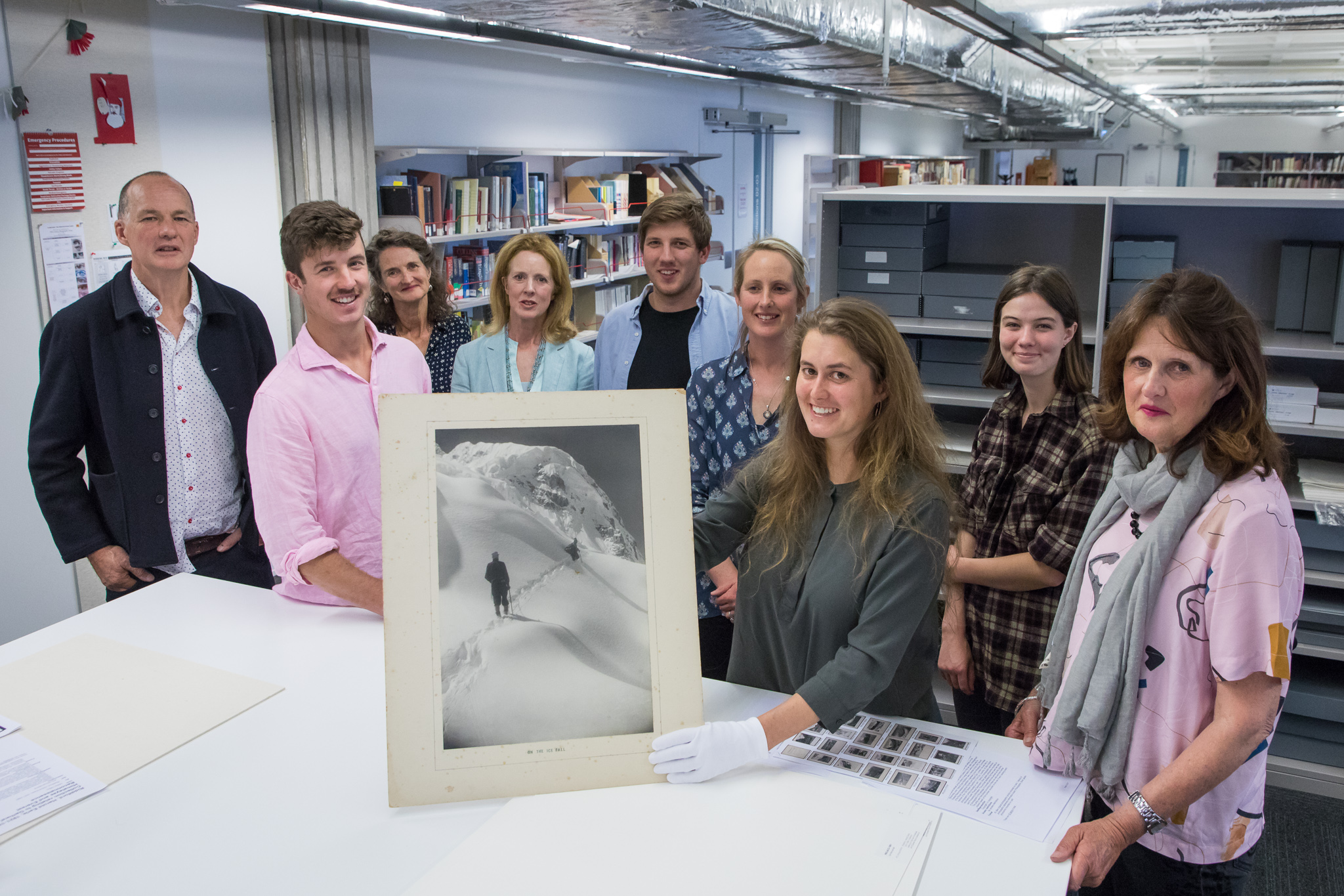 Shows the Riddiford family standing around Catherine Bisely who is holding a large black and white print.
