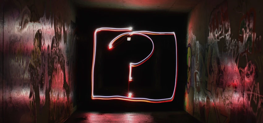 An illuminated square containing an illuminated question mark set in a dark tunnel.