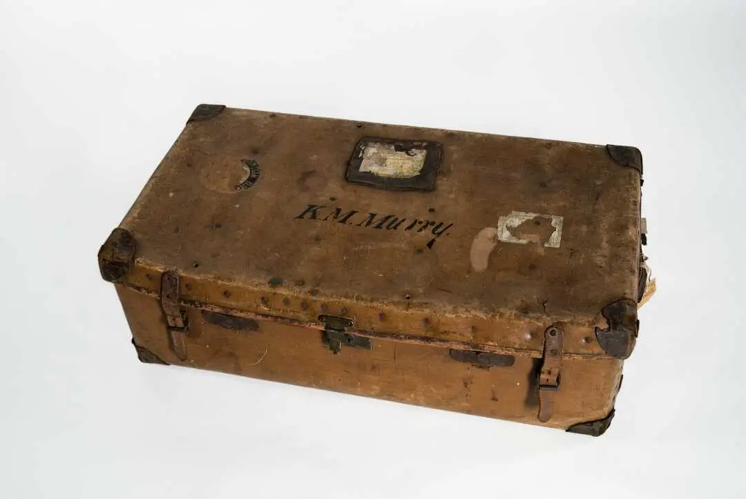 A worn brown leather suitcase with the letters "K.M. Murry" on the outside.