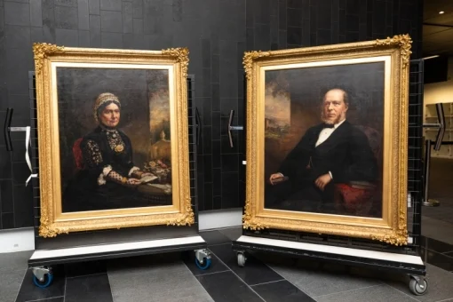 Two portraits with large gold frames are seen on easels.