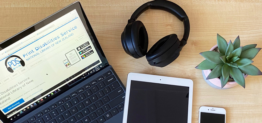 Laptop with Print Disabilities Service Wheelers platform on the screen alongside headphones and other digital devices