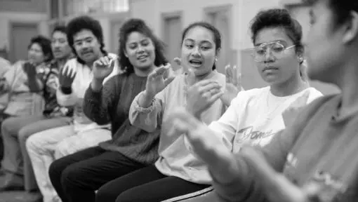 A row of people appear to be singing and making coordinated hand gestures. 