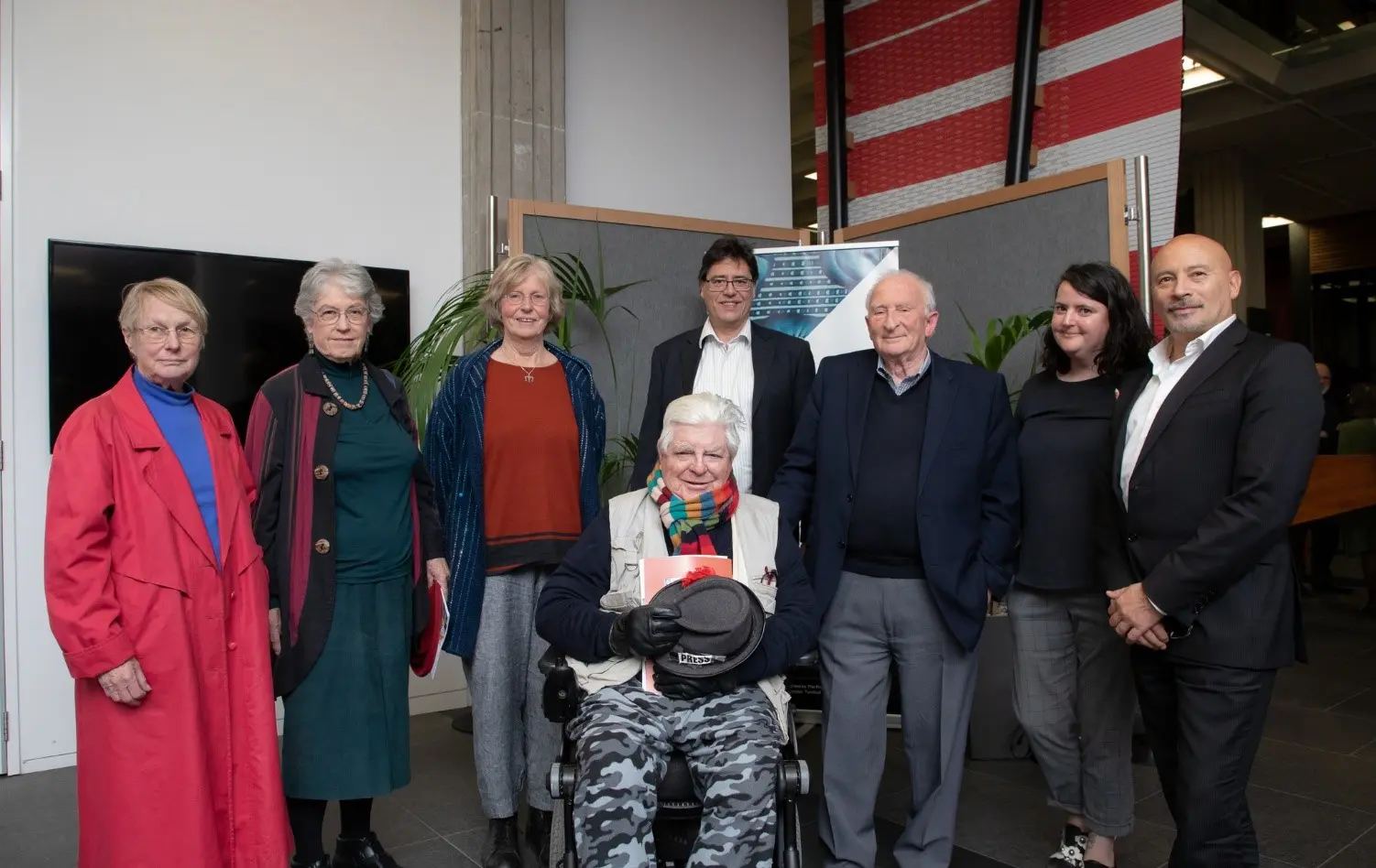 Shows a group portrait with Bob Brockie seated in a wheelchair in the middle of the group who are standing.