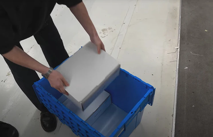 A box being put into a blue plastic packing crate. 