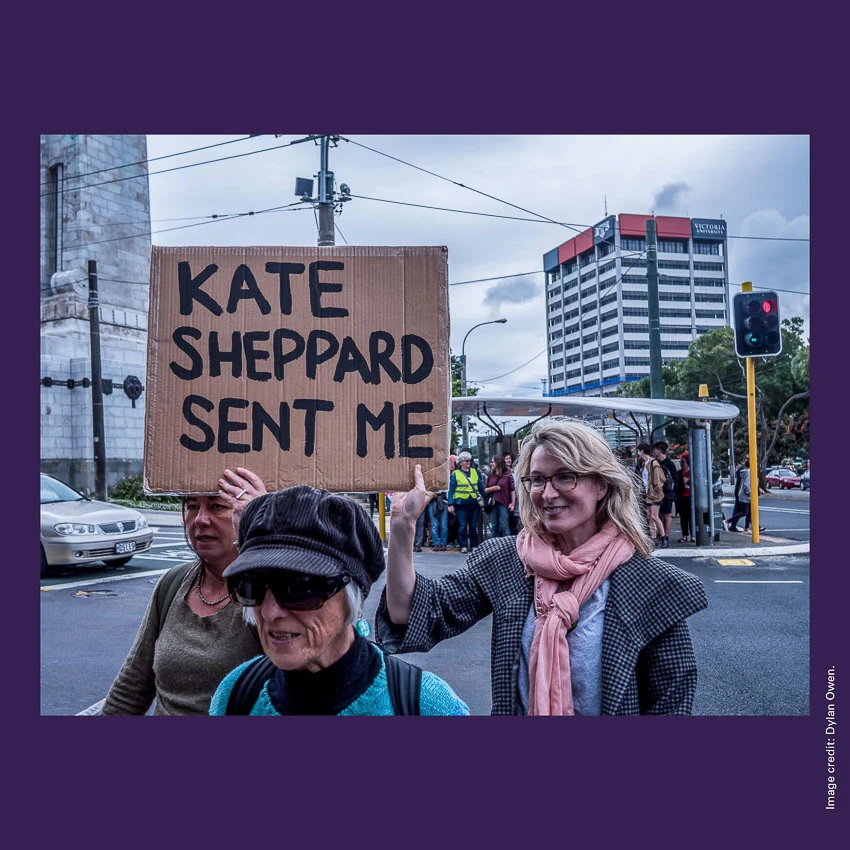 Front of curiosity card CC0007 with an image of women marching in Wellington and holding a sign with the words 'KATE SHEPPARD SENT ME'.