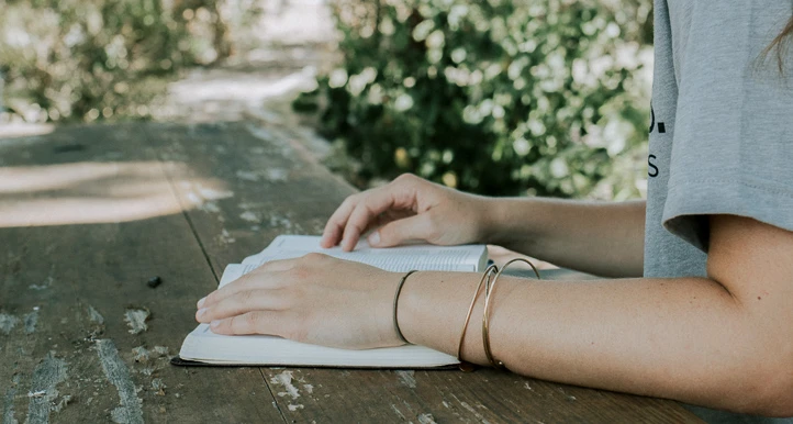 Young person's hands holding open book on a table outside