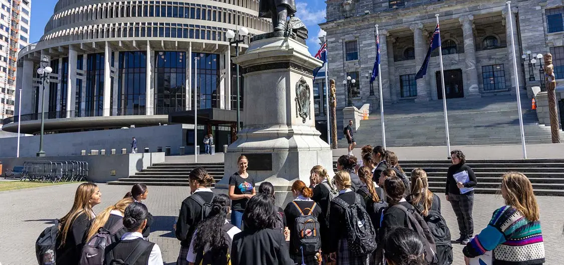 Group of students with learning facilitators on Parliament's grounds with Parliament buildings in the background.