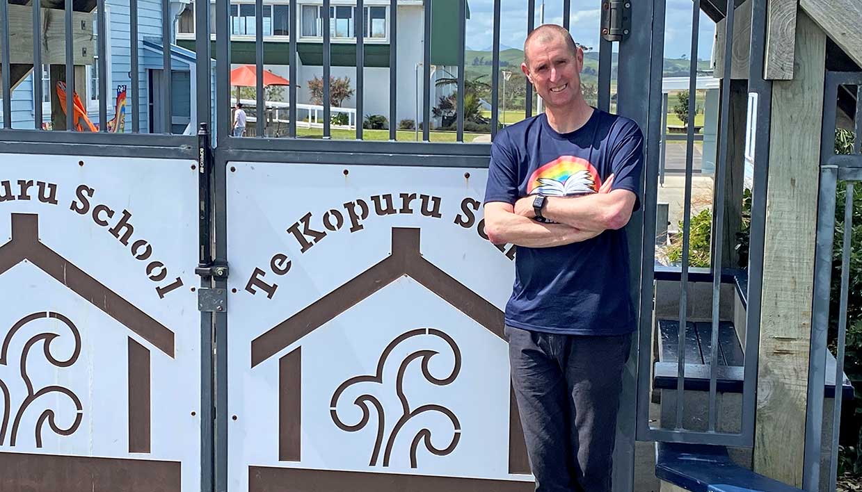 Te Awhi Rito Alan Dingley smiling and standing by the Te Kopuru School gate.