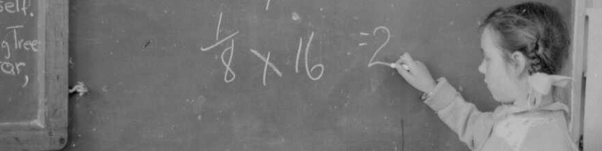 Black and white photo of young girl with plaited hair doing a maths equation on a chalk board. 