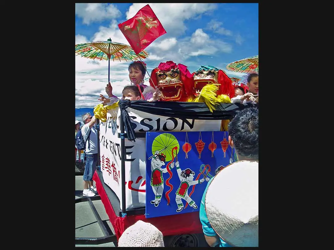 Colour photo of a Chinese New Year celebration. It shows performers, including 2 lion figures, and people watching.