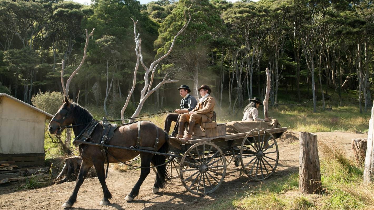 A horse-drawn carriage carrying three men is moving along a dirt road.