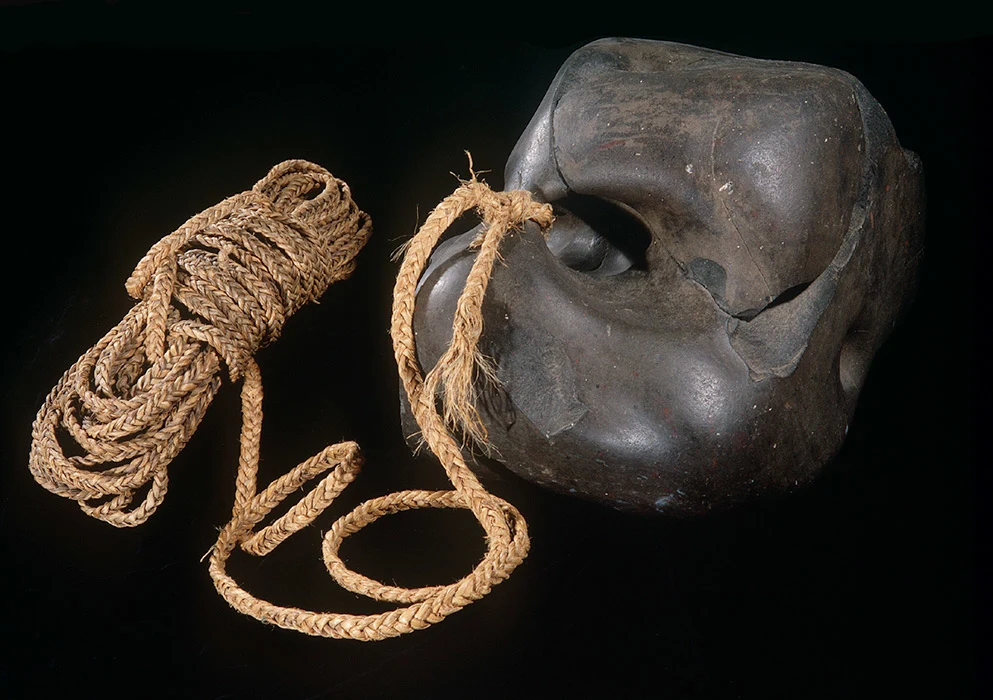 Colour studio photograph of a punga (anchor stone) tied to a rope coil.