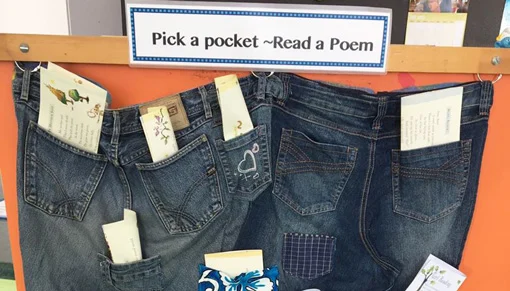 A sign 'Pick a pocket — Read a Poem' above a display of jeans hanging on a wall with poetry sticking out of the pockets  
