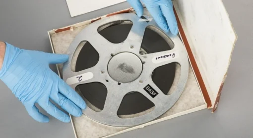 Hands wearing rubber gloves are displaying a magnetic reel of tape. 