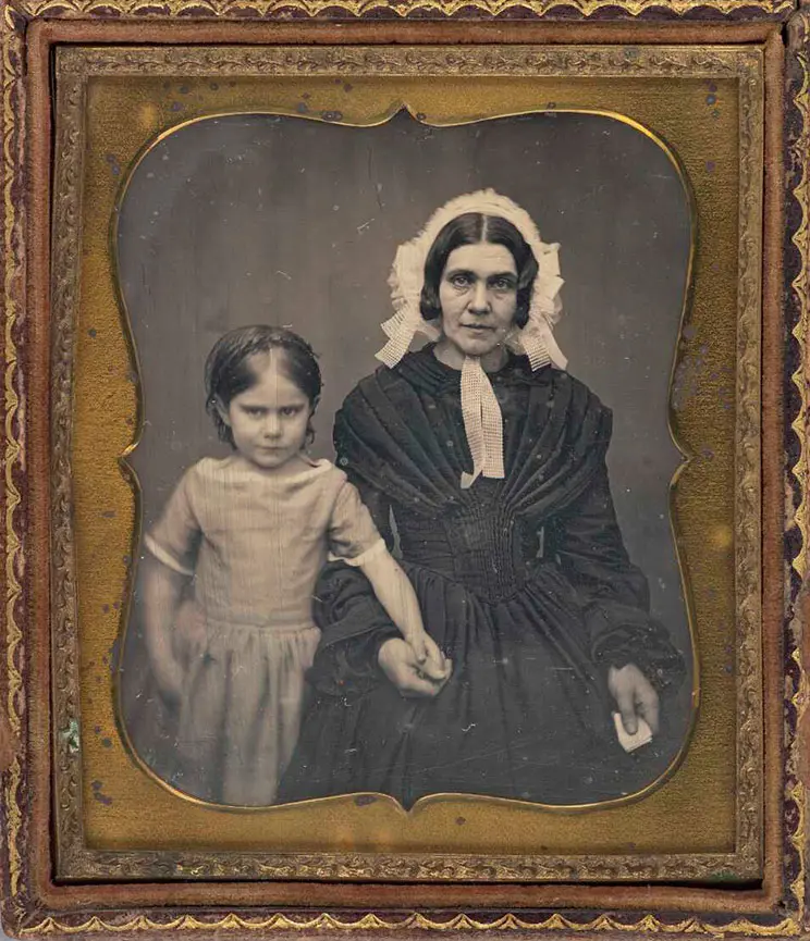 Woman and child. Woman is holding child's hand. Both look reticent about being photographed. 