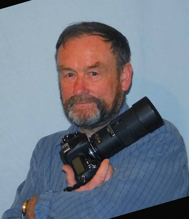Headshot portrait of a man holding a digital camera.