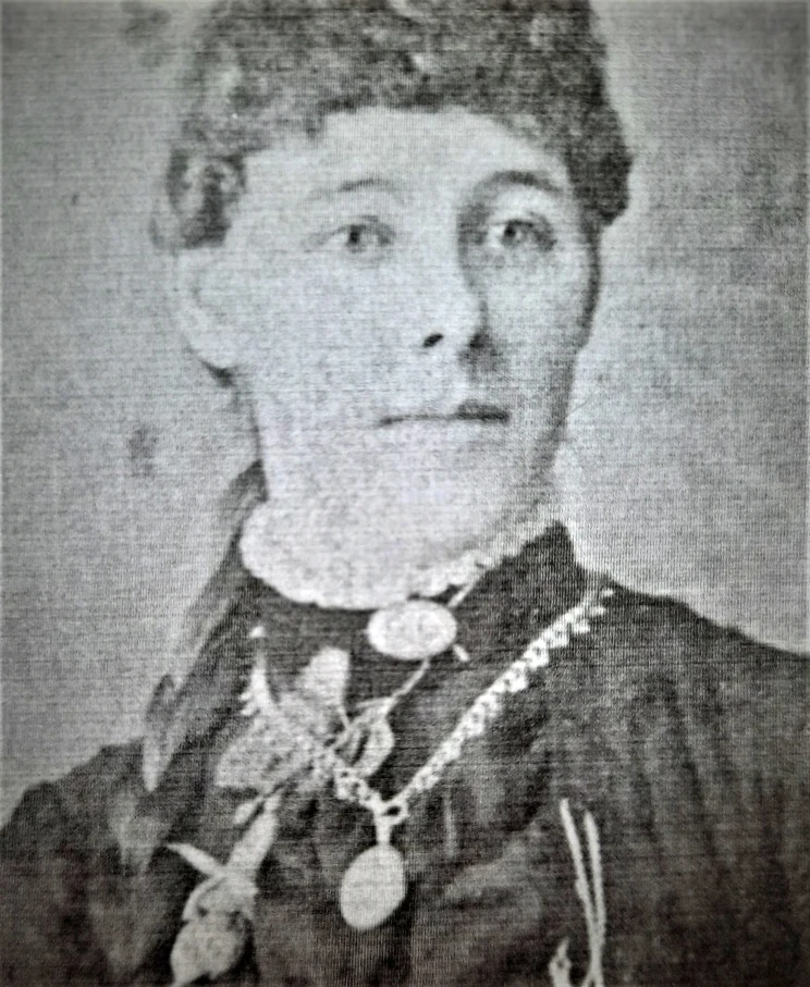 A black and white portrait of a woman wearing high collar and necklace with pendant.