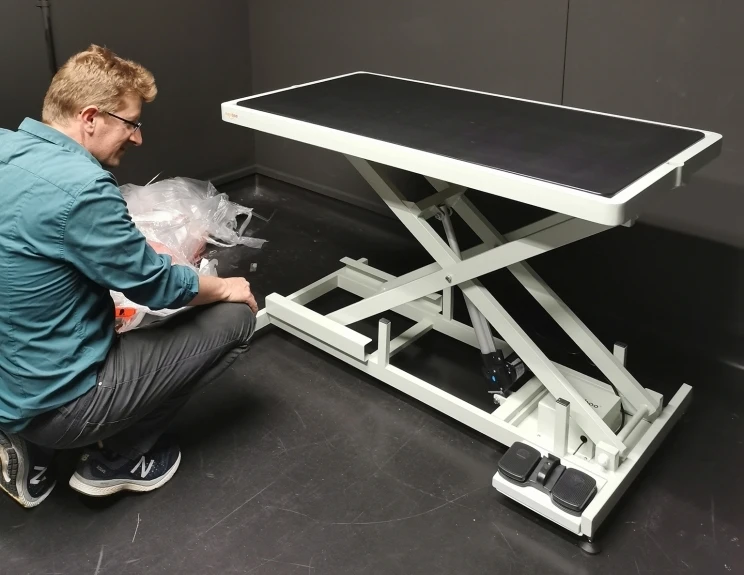 A technician crouches before a large, metal platform that can be raised and lowered mechanically.