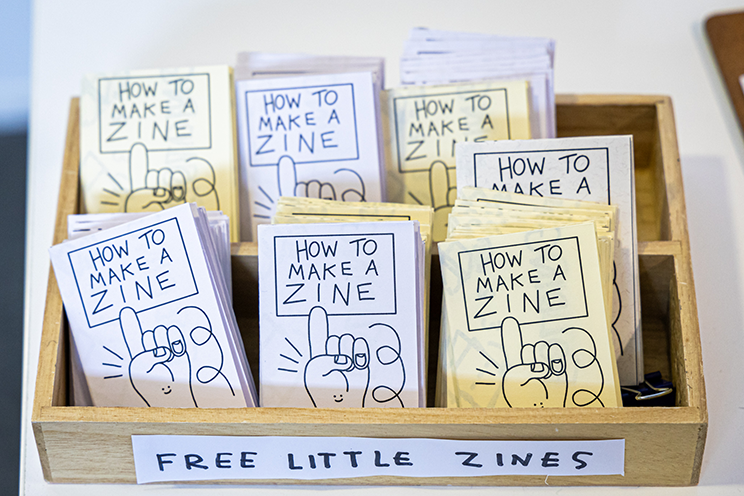 Wooden box with label "Free little zines". In the box are small pamphlets with the title "How to make zine".