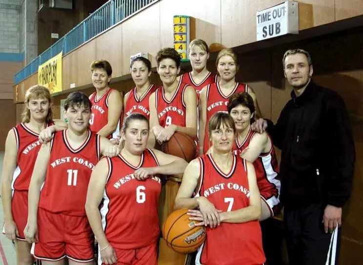 A women's basketball team photo with team members wearing red uniforms and the male coach in black.