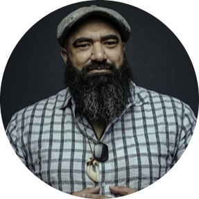 Head and shoulders photo of a Māori man wearing a pounamu and a bone hei matau.