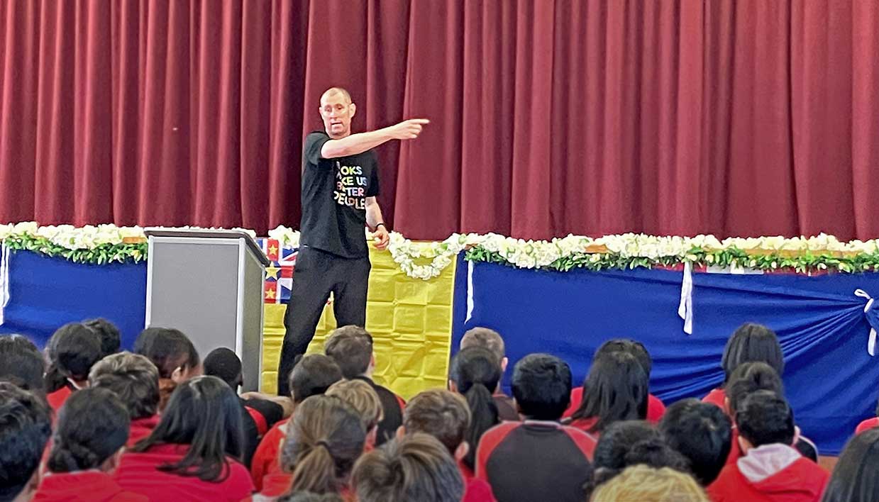 Te Awhi Rito Reading Ambassador Alan Dingley speaking on stage to a group of students.