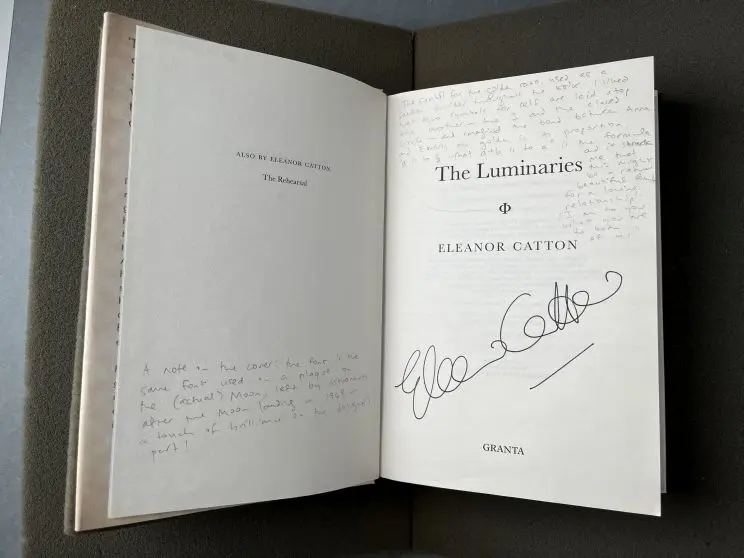 A book open to the title page shows an author's signature in black ink along with notes written in the margins in pencil of both pages.