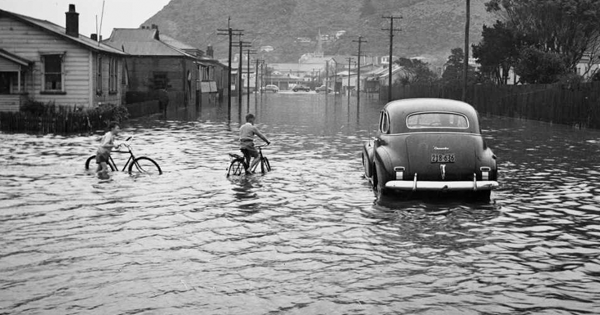 A car and two children on bicycles in a flooded street. 