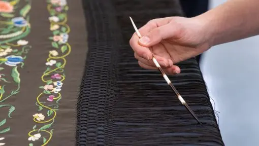 A hand is shown separating fine tassels on a delicate silk shawl. 