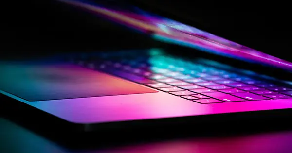 Photo of purple and blue lights shining on a partially open laptop.