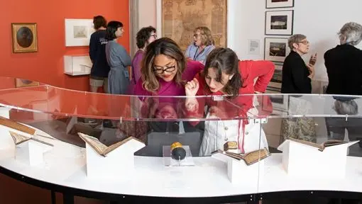 Two women lean over a display case admiring the objects within. 