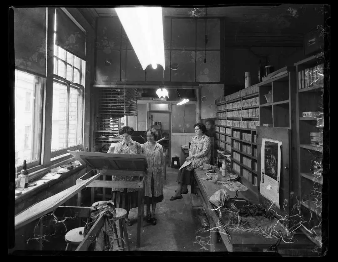 Shows three women in a workroom, most likely colourising b&w photographs.