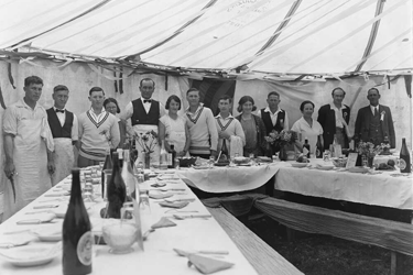 Black and white photo of people around a table laid for a feast. 