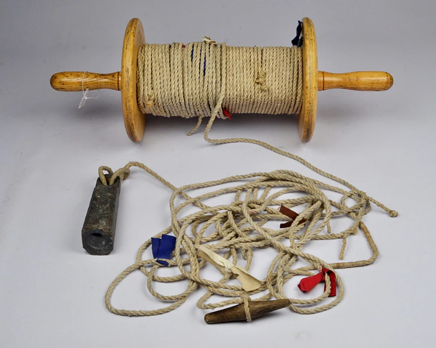 Colour studio photograph of a lead line. It shows a reel partially uncoiled with coloured markers along the line and a metal weight on the end.