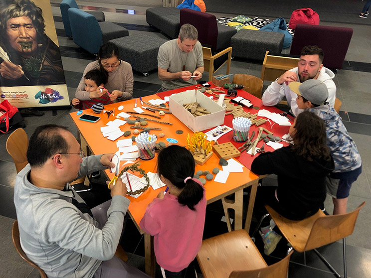 Group of people sitting around a table making taonga pūoro.