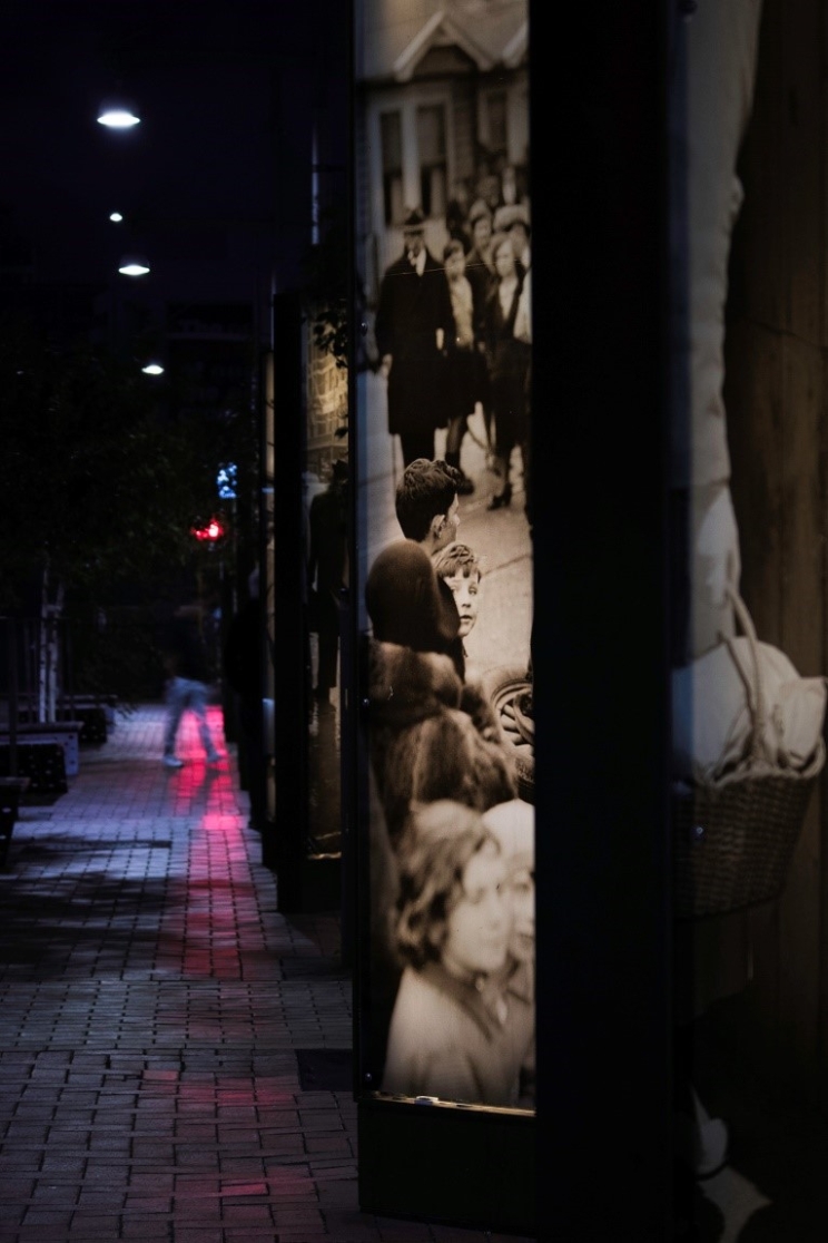 A street scene at night showing a vertical black and white image that is illuminated from within using a lightbox.