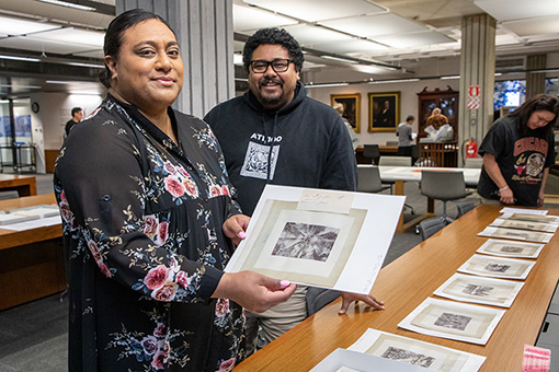 Three people looking at copies of black and white photos on a table in a library reading room.