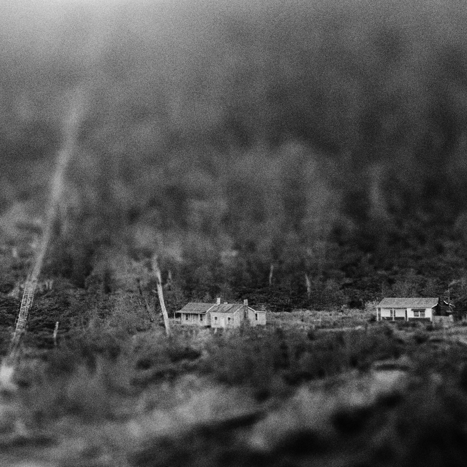 View from the distance of a house and surrounding buildings all set amongst trees.
